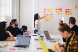 A presenter in a meeting looks at post-its hanging against the wall that are the result of a brainstorming session.
