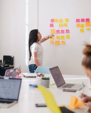 A presenter in a meeting looks at post-its hanging against the wall that are the result of a brainstorming session.