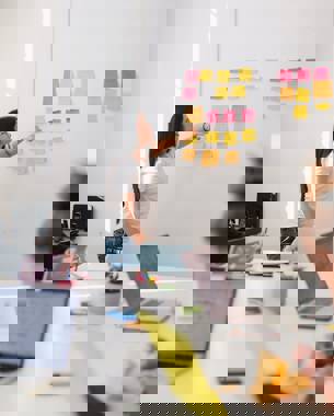 Een presentator in een vergadering kijkt naar post-its die tegen de muur hangen en het resultaat zijn van een brainstormsessie.