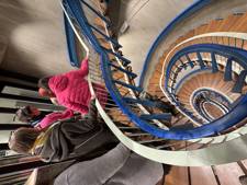 A group of people descending a spiral staircase with wooden steps and a blue railing.