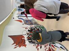 A group of people is viewing a colorful mural depicting a historical scene with flags and figures in a modern space.