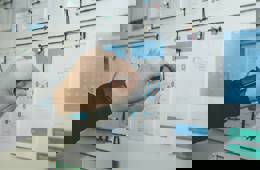 Op een whiteboard staan een aantal uitgeprinte documenten en een persoon verbindt lijnen daartussen met behulp van een draad.