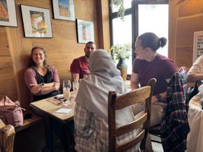 A group of people in a cozy restaurant setting, with drinks on the table and natural light.
