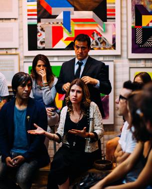 photo of a group of people sitting in a semicircle facing the camera. one of them has the floor.